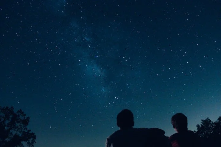 Two people stargazing under a starry night sky.