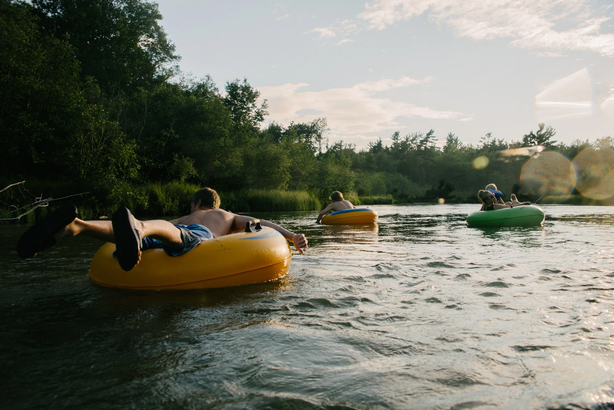 People tubing on a river during sunset with lush trees along the banks.