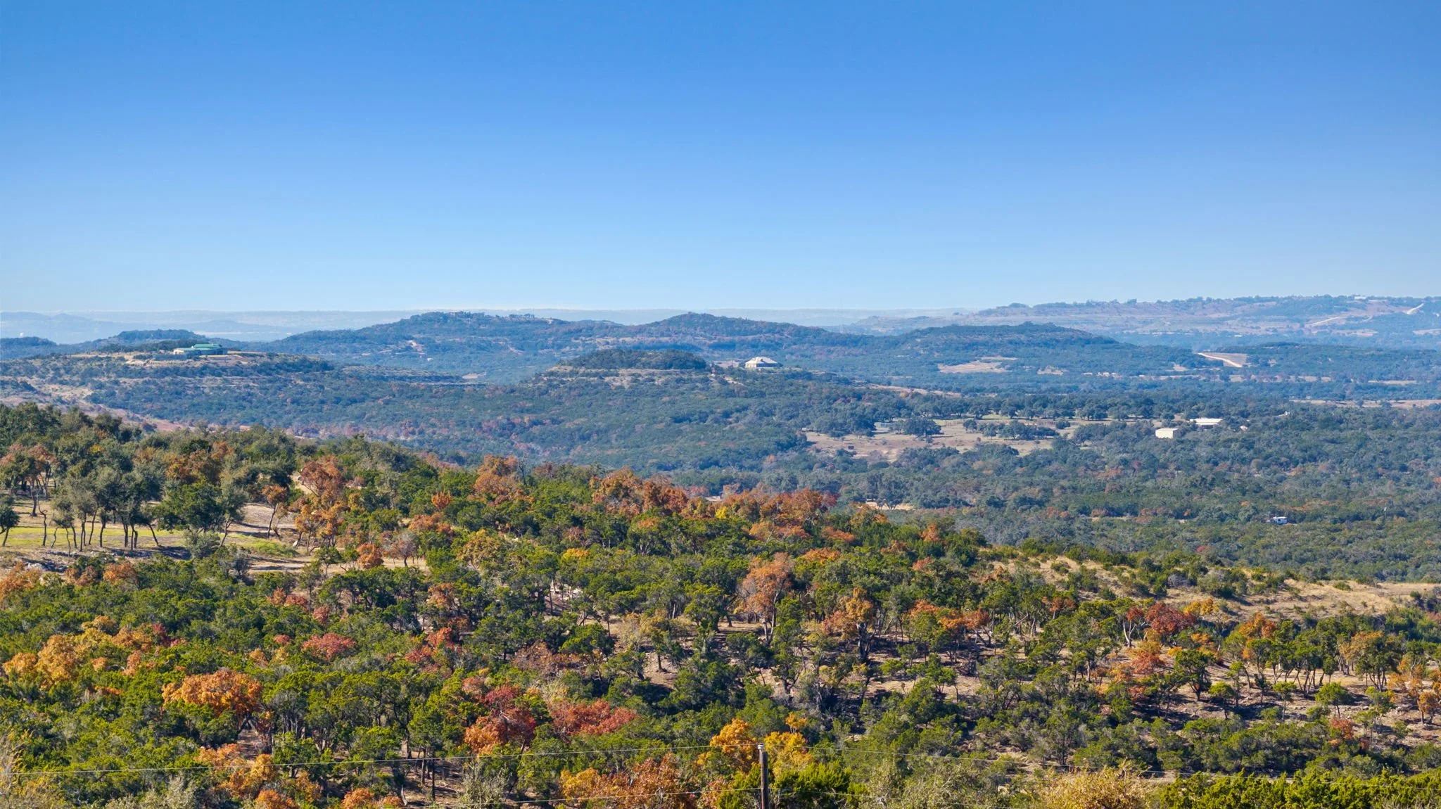 A scenic view of rolling hills covered with trees in autumn colors under a clear blue sky.